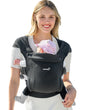 Smiling woman wearing charcoal grey ergonomic baby carrier with baby nestled inside. Product page.