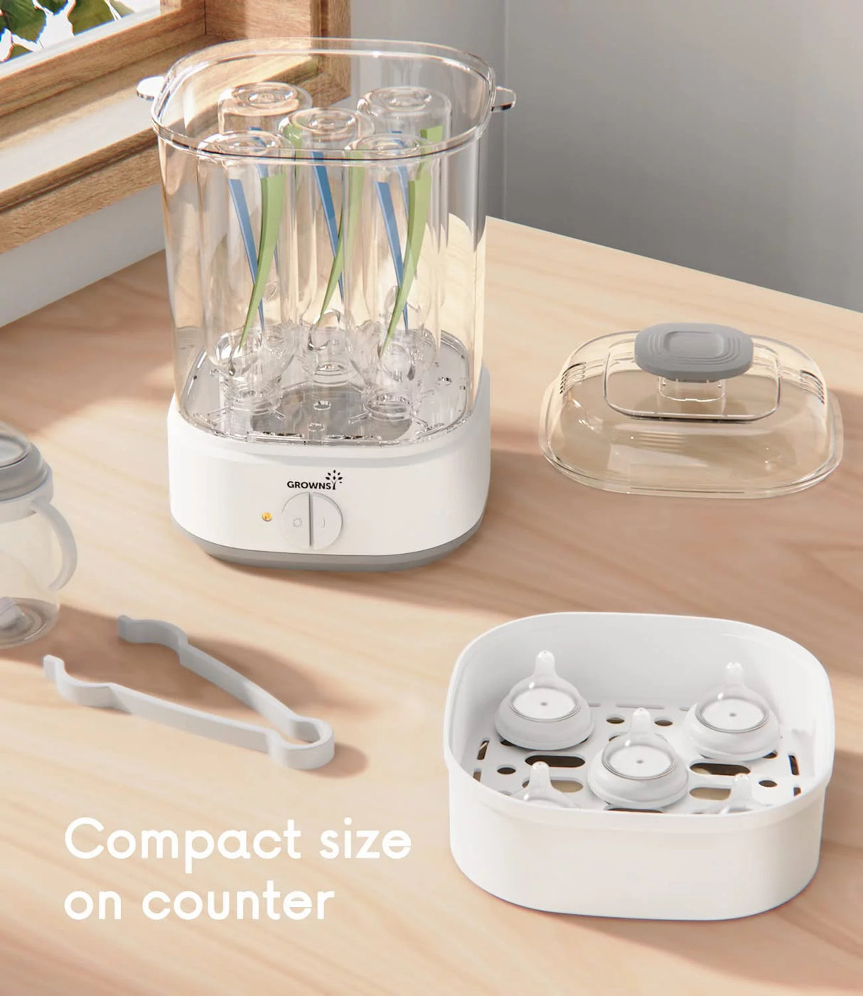 White Grownsy electric baby bottle sterilizer with pacifiers and bottle nipples shown on a kitchen counter.