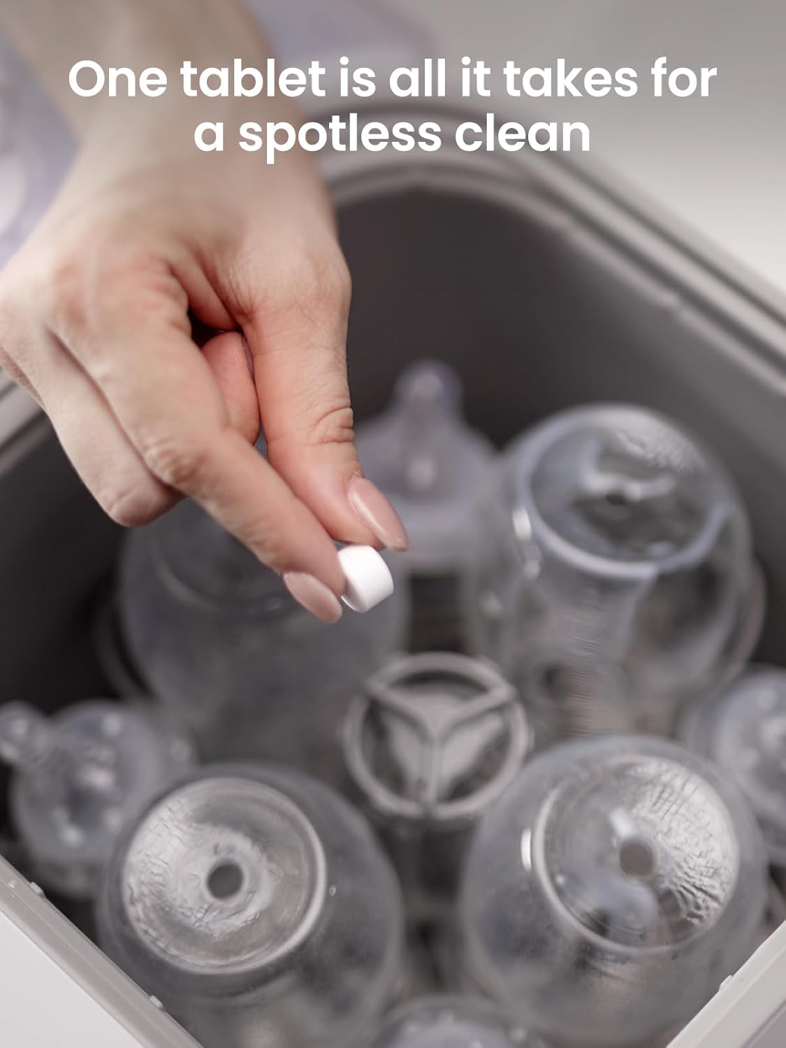 Hand dropping GROWNSY bottle washer detergent tablet into rack of baby bottles for spotless clean.