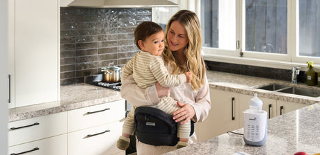 Mother holding baby in kitchen with GROWNSY baby bottle warmer on countertop