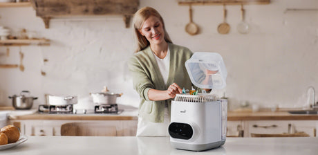 A mother places a bottle into a sterilizer in the kitchen, ensuring safe and hygienic feeding.