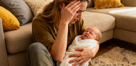 Tired mother comforting crying baby on living room couch, GROWNSY baby care support