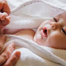 Close-up of a newborn baby being gently wrapped in a soft white towel by a parent's hands