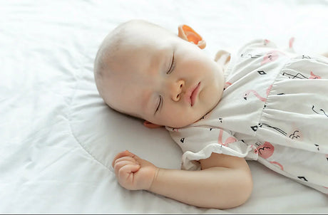 A 6-month-old baby sleeping on a bed