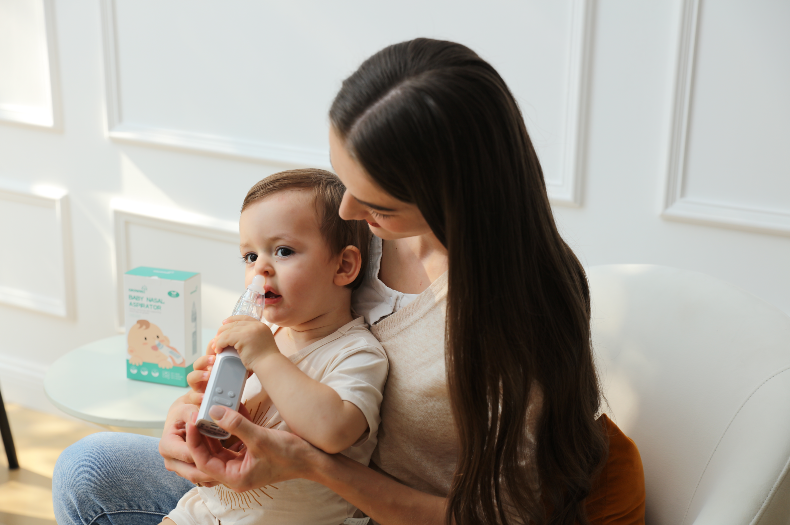 Mother holding a baby and using an electric nasal aspirator to clear the infant's nose.