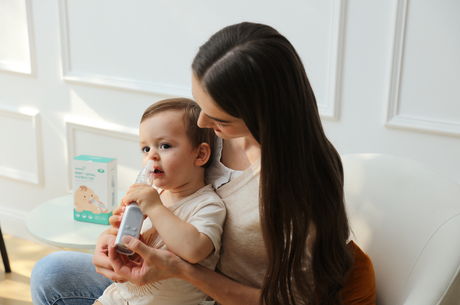 Mother holding a baby and using an electric nasal aspirator to clear the infant's nose.