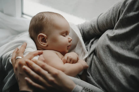 Sleeping baby held close against a parent’s chest.