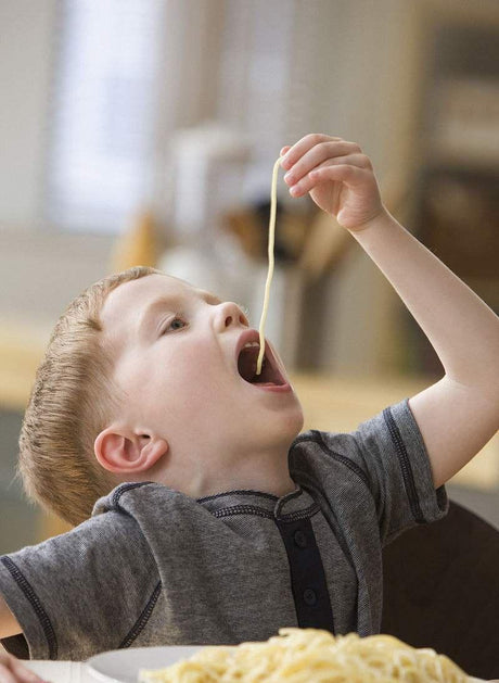 Young boy eating spaghetti by dangling a long noodle into his open mouth
