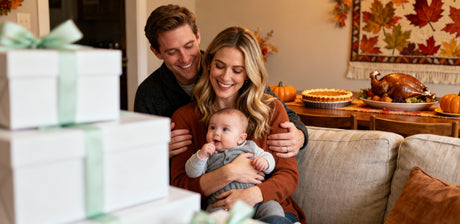 A family celebrates Thanksgiving together, with a baby on the lap and gifts nearby.