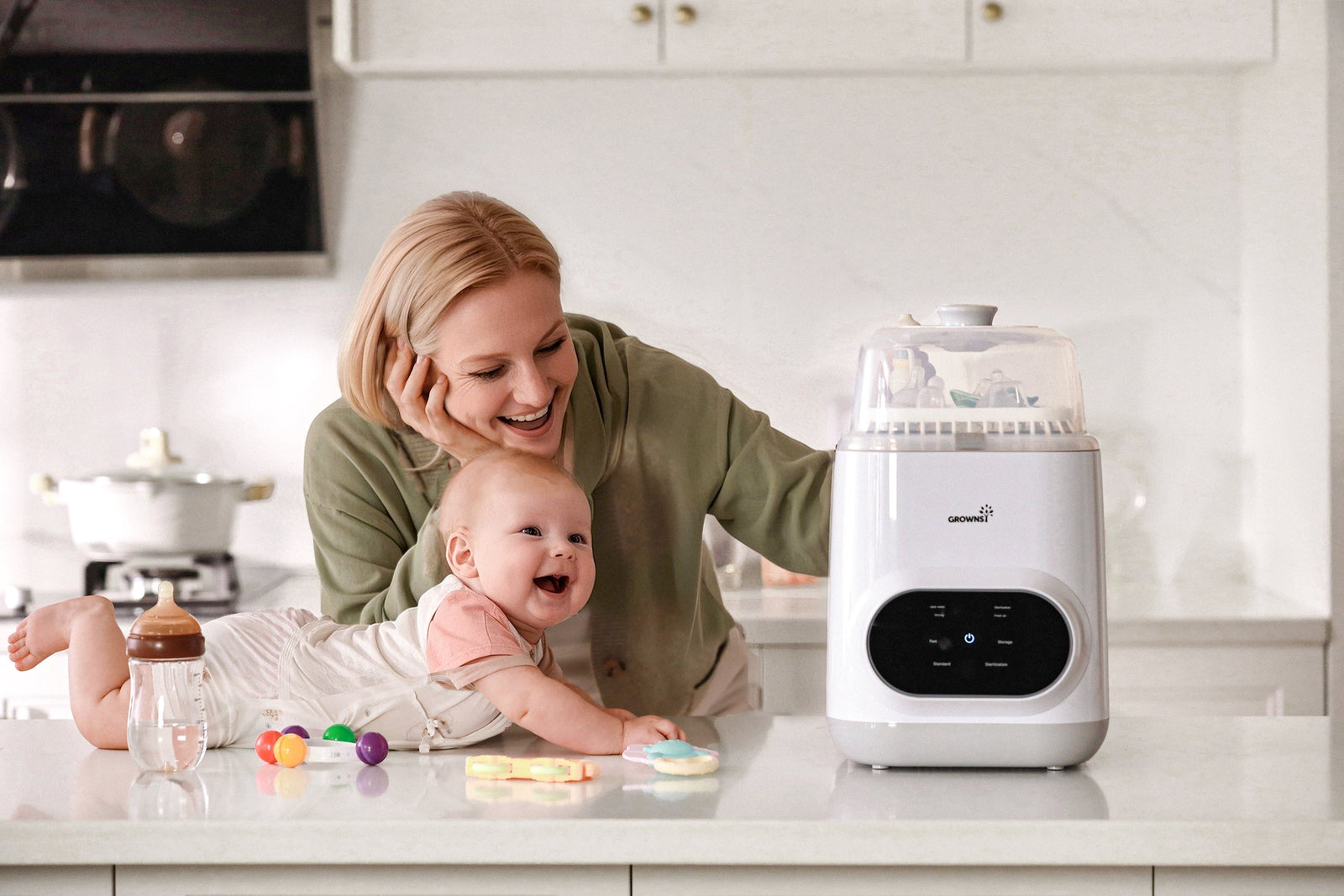 A joyful mother and her happy baby playing beside a Grownsy automatic baby bottle washer and sterilizer on a kitchen counter