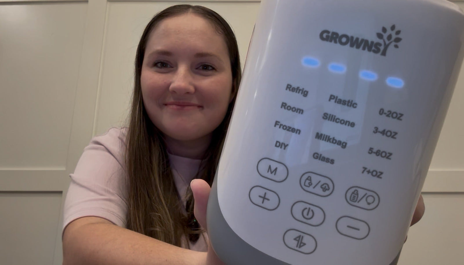 A mother holds a Grownsway bottle warmer, displaying its digital controls and temperature settings for safe feeding.