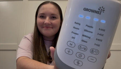 A mother holds a Grownsway bottle warmer, displaying its digital controls and temperature settings for safe feeding.