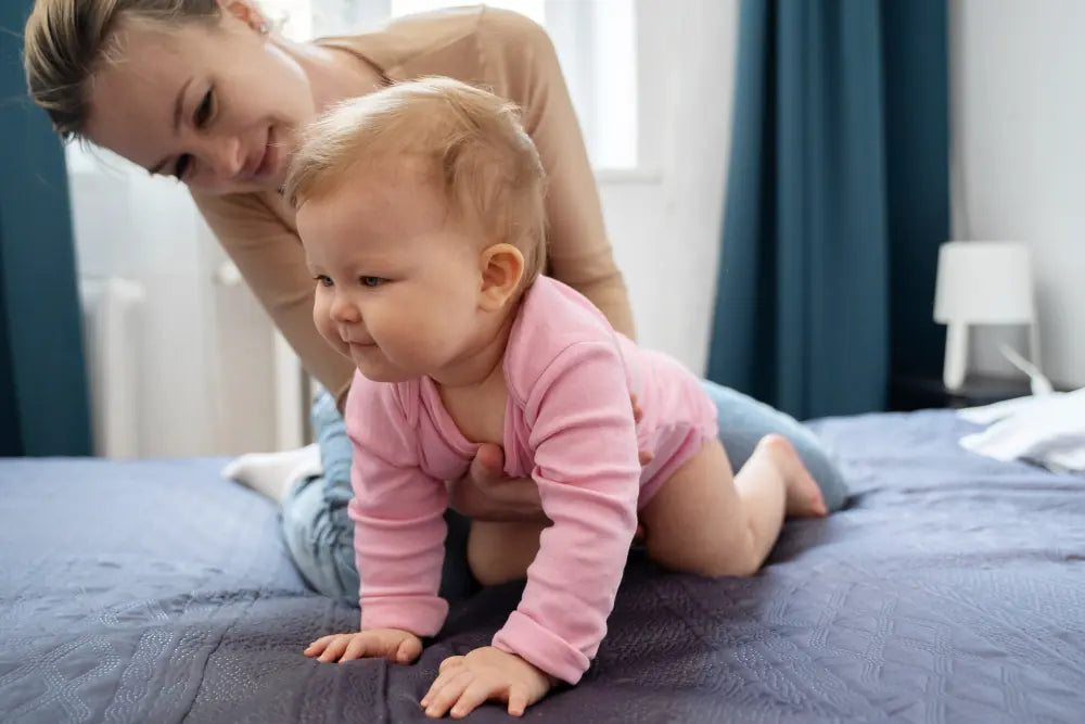 Mother supports her baby during crawling practice on a bed.